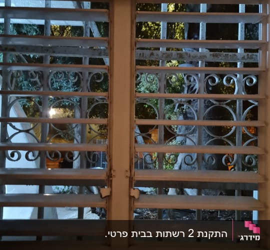 חלון עם סורגים מתכתיים ועצים ברקע